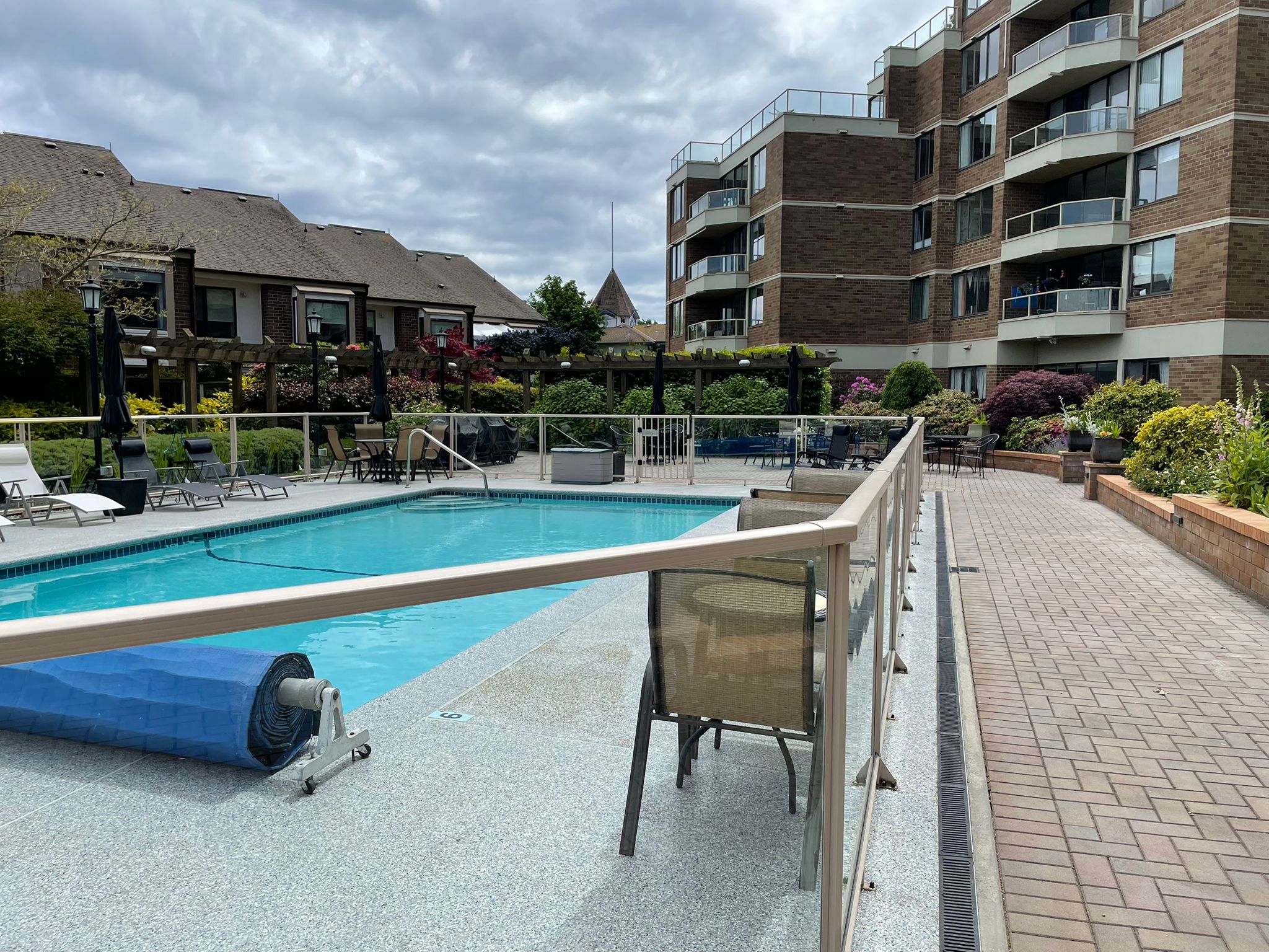 2225belleville14 | Apartments Homes Suites for Rent Victoria BC Outdoor pool area at a residential complex with lounge chairs and glass railing brick buildings and cloudy sky above