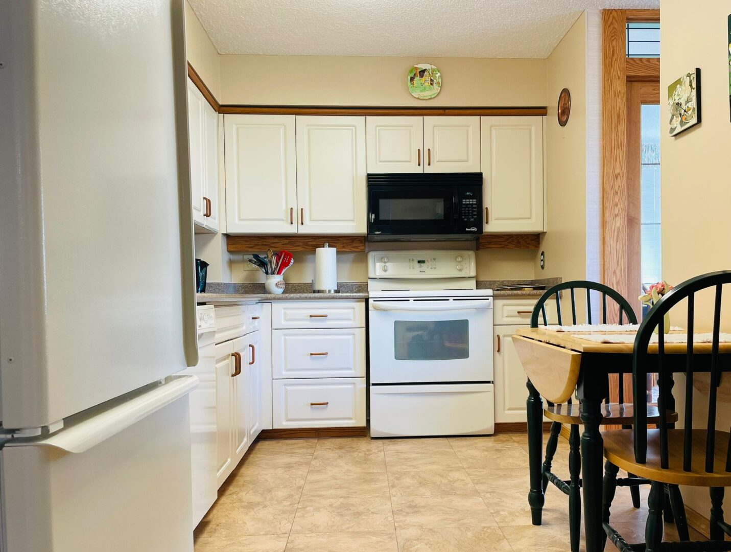 2225belleville7 | Apartments Homes Suites for Rent Victoria BC Bright kitchen with white cabinets a black microwave above a white stove and beige walls with wooden trim In the foreground a dining table and green chairs are visible on the right
