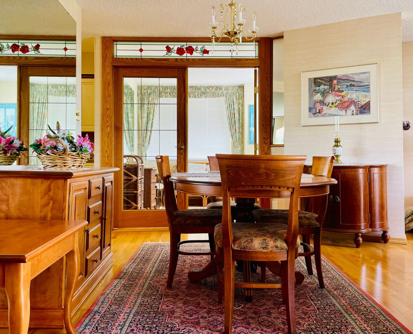 225belleville1 | Apartments Homes Suites for Rent Victoria BC Wood dining area with a long wooden table matching chairs and a floral centerpiece glass paneled doors and a stained glass transom above
