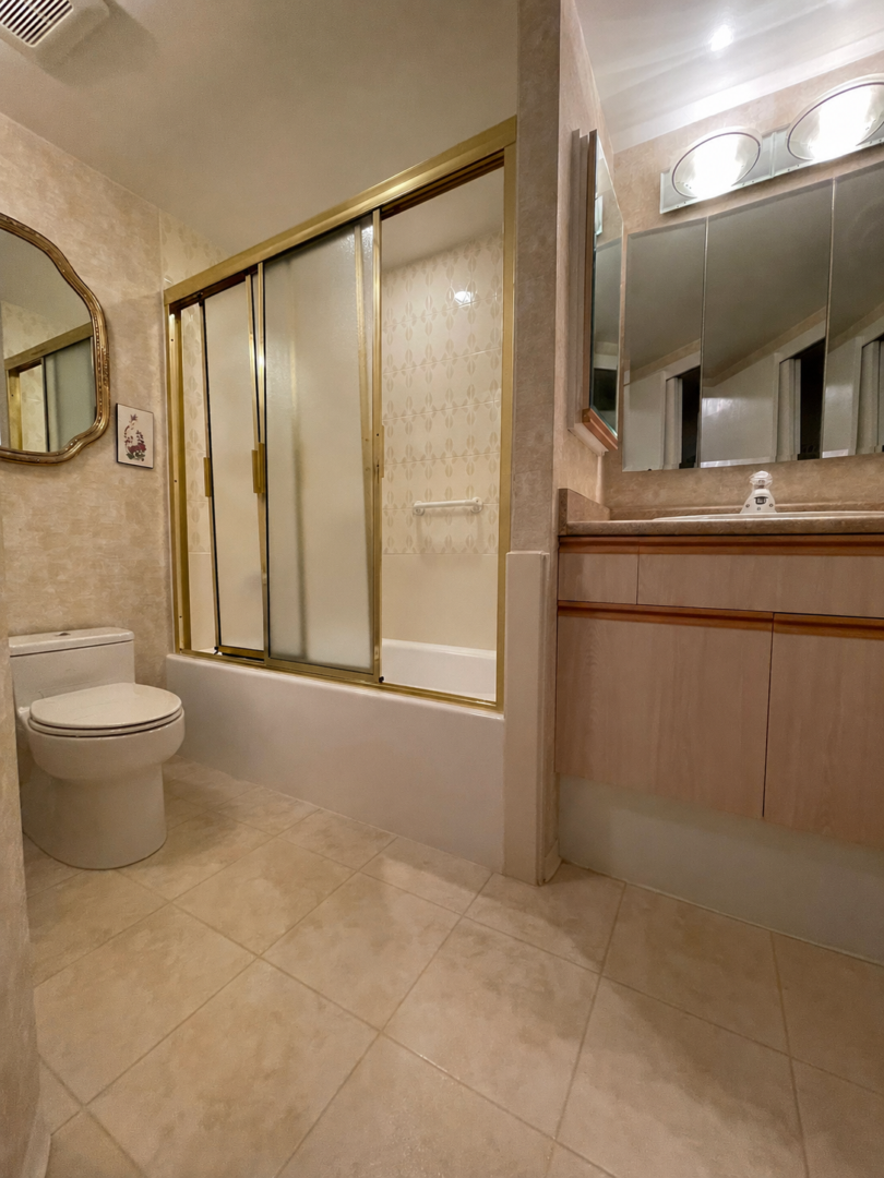 225belleville15 | Apartments Homes Suites for Rent Victoria BC Bathroom with a beige tiled floor toilet on left and a sliding glass shower door with brass frame in the center left
