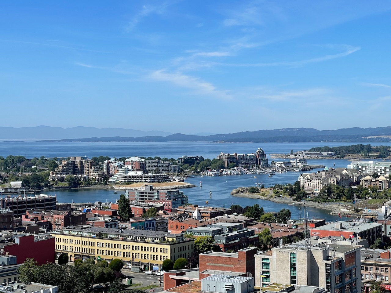 Aerial view of a harbor town with boats in a marina mixed red brick and beige buildings and distant mountains under a blue sky