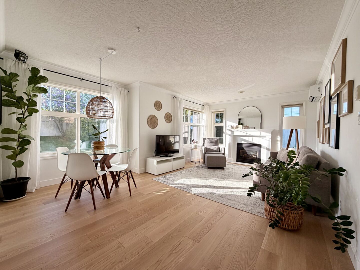 Bright open concept livingdining room with glass round table white chairs and large windows letting in natural light Green plants add life to the space