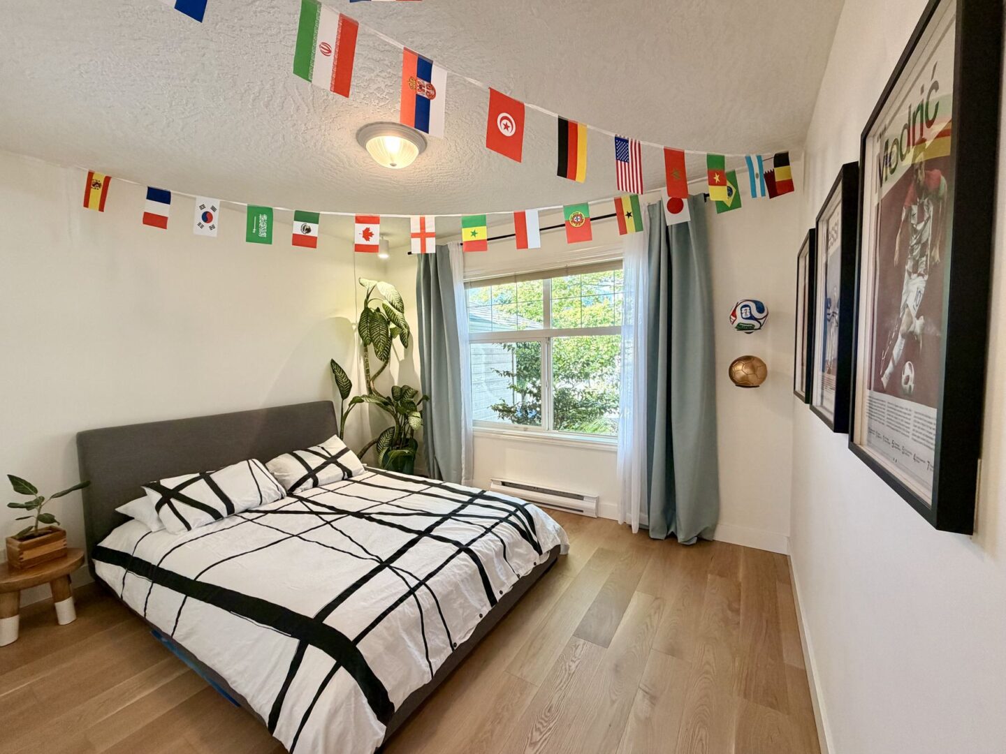 Bedroom with flag bunting across the ceiling a bed with a black and white geometric duvet and a leafy plant by the window