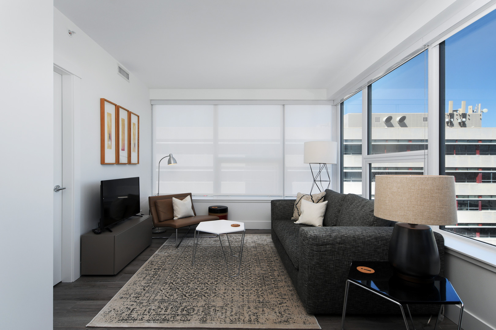 110638 | Apartments Homes Suites for Rent Victoria BC Modern living room with gray sofa brown chair coffee table and framed artwork under a bank of large windows