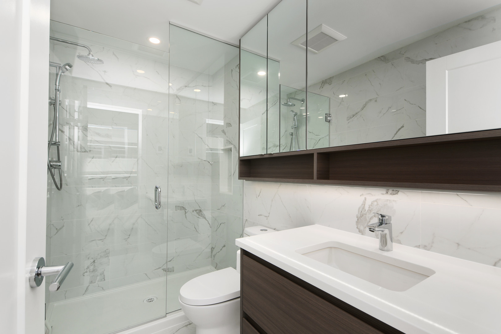110645 | Apartments Homes Suites for Rent Victoria BC Modern bathroom with glass enclosed shower marble walls and white countertop sink with dark wood vanity panels