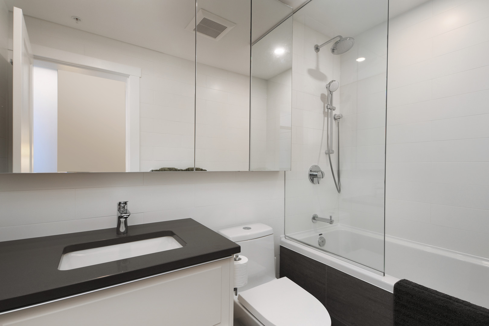 110647 | Apartments Homes Suites for Rent Victoria BC Modern bathroom with a dark countertop sink mirrored cabinet white tiles and a glass enclosed bathtubshower combo