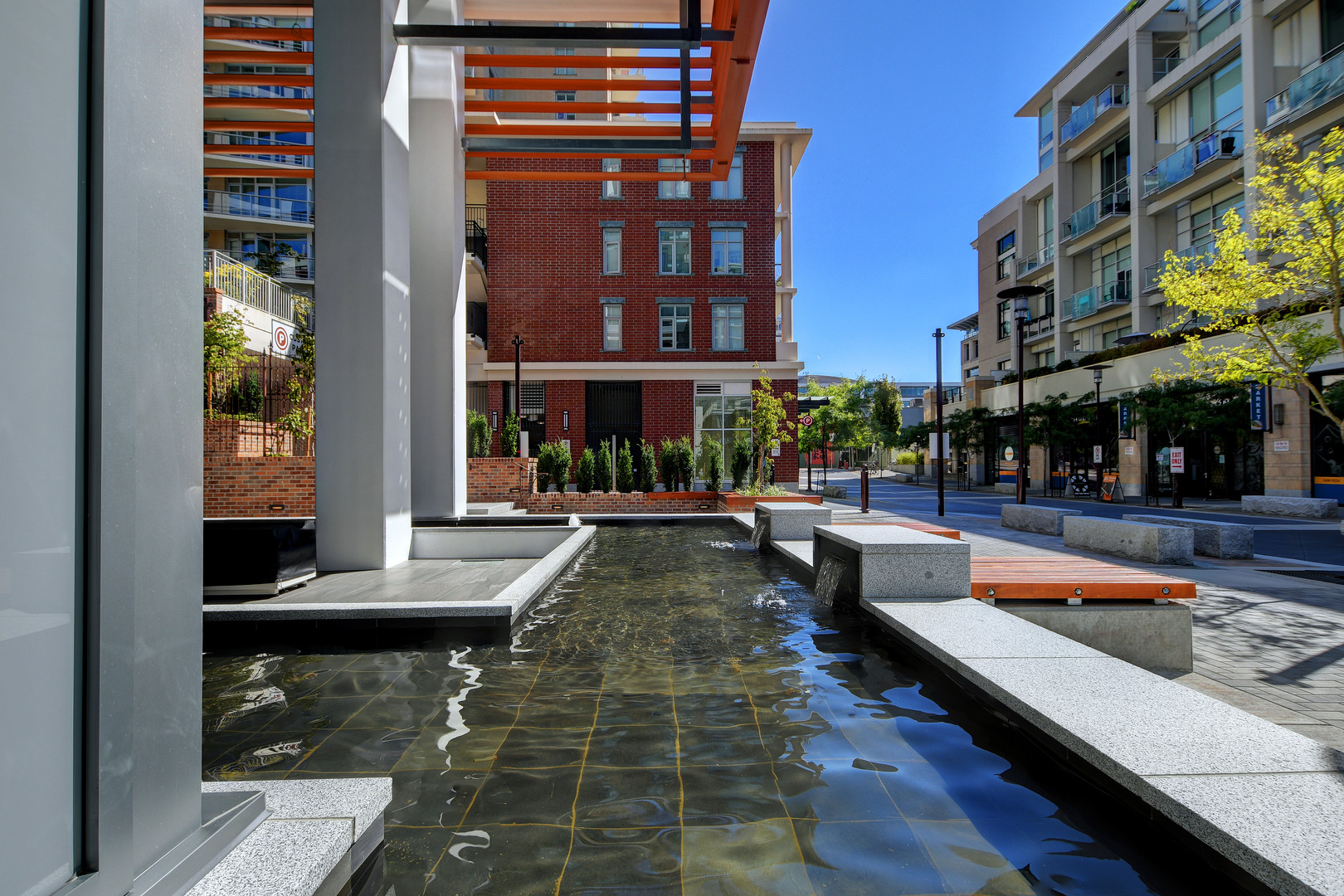 110653 | Apartments Homes Suites for Rent Victoria BC Wide view of a modern urban plaza with a shallow water feature concrete benches and a red brick building behind the scene