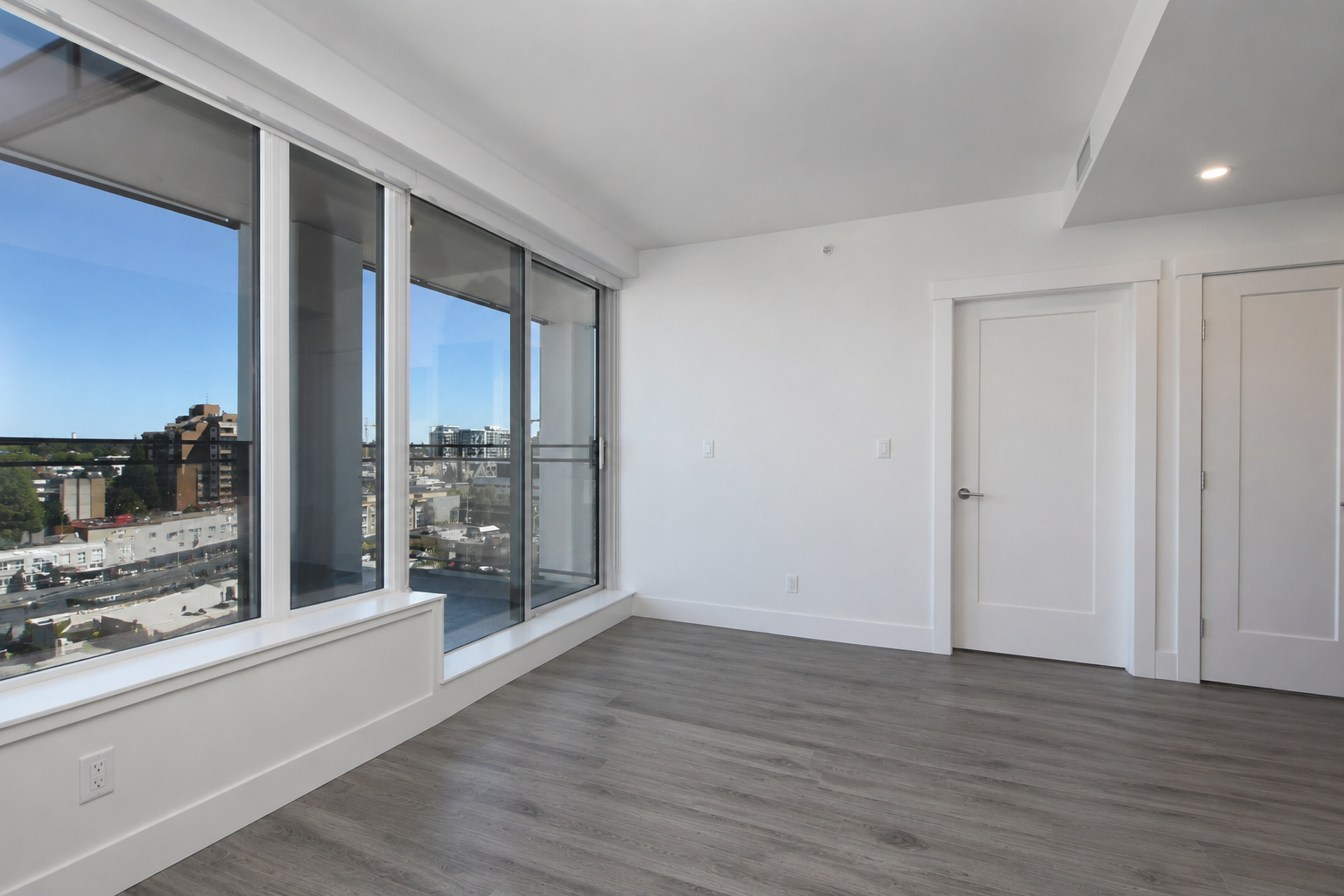 1106livingspace01 | Apartments Homes Suites for Rent Victoria BC Bright empty living room with large floor to ceiling windows overlooking the city gray wood flooring and white walls