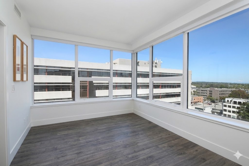 1106livingspace04 | Apartments Homes Suites for Rent Victoria BC Bright corner room with large window walls white walls and gray wood flooring overlooking a distant cityscape