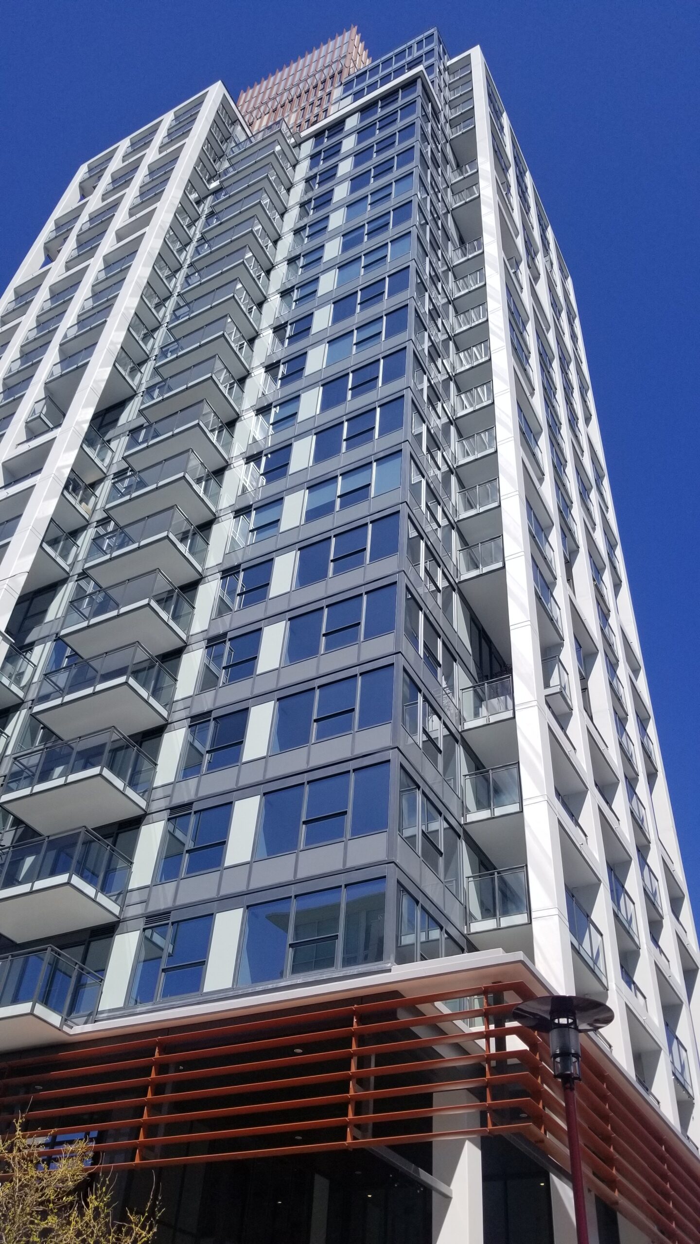 20200715153002 | Apartments Homes Suites for Rent Victoria BC Tall modern glass apartment building with numerous balconies against a clear blue sky photographed from below