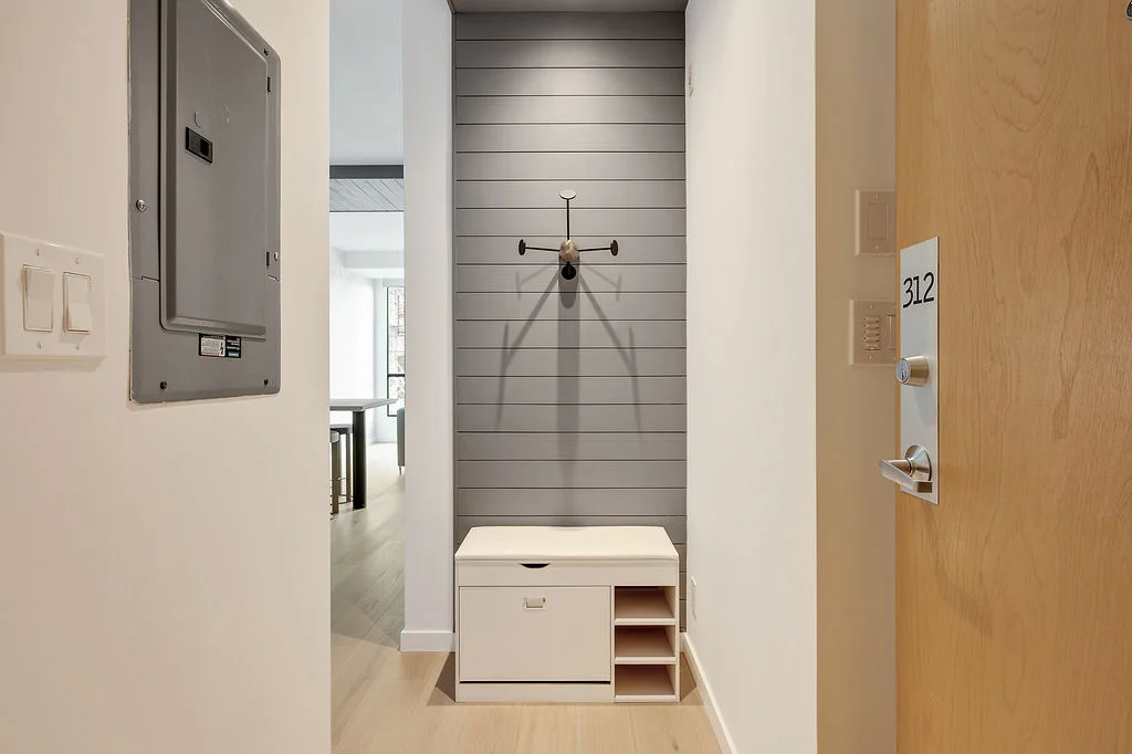 Entry alcove with gray shiplank wall wall hook and a white storage bench with cubbies for shoes beneath a small seat