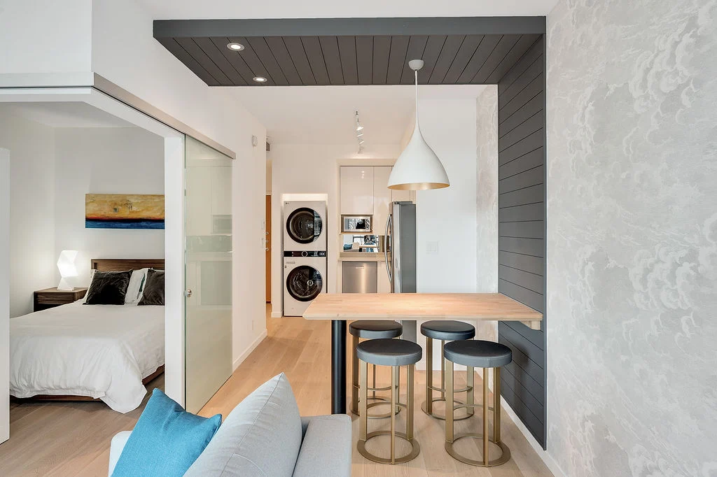 312 409 Swift5 | Apartments Homes Suites for Rent Victoria BC Open plan living area with a wooden kitchen island and four gray bar stools a gray accent wall and a view into a bedroom with a sliding glass door to the left