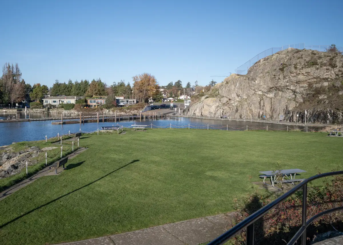 Lakeside park scene with green lawn calm water a rocky hill on the right and a picnic table in the foreground