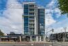 Modern six story glass front condo building with balconies on a busy street storefronts at ground level