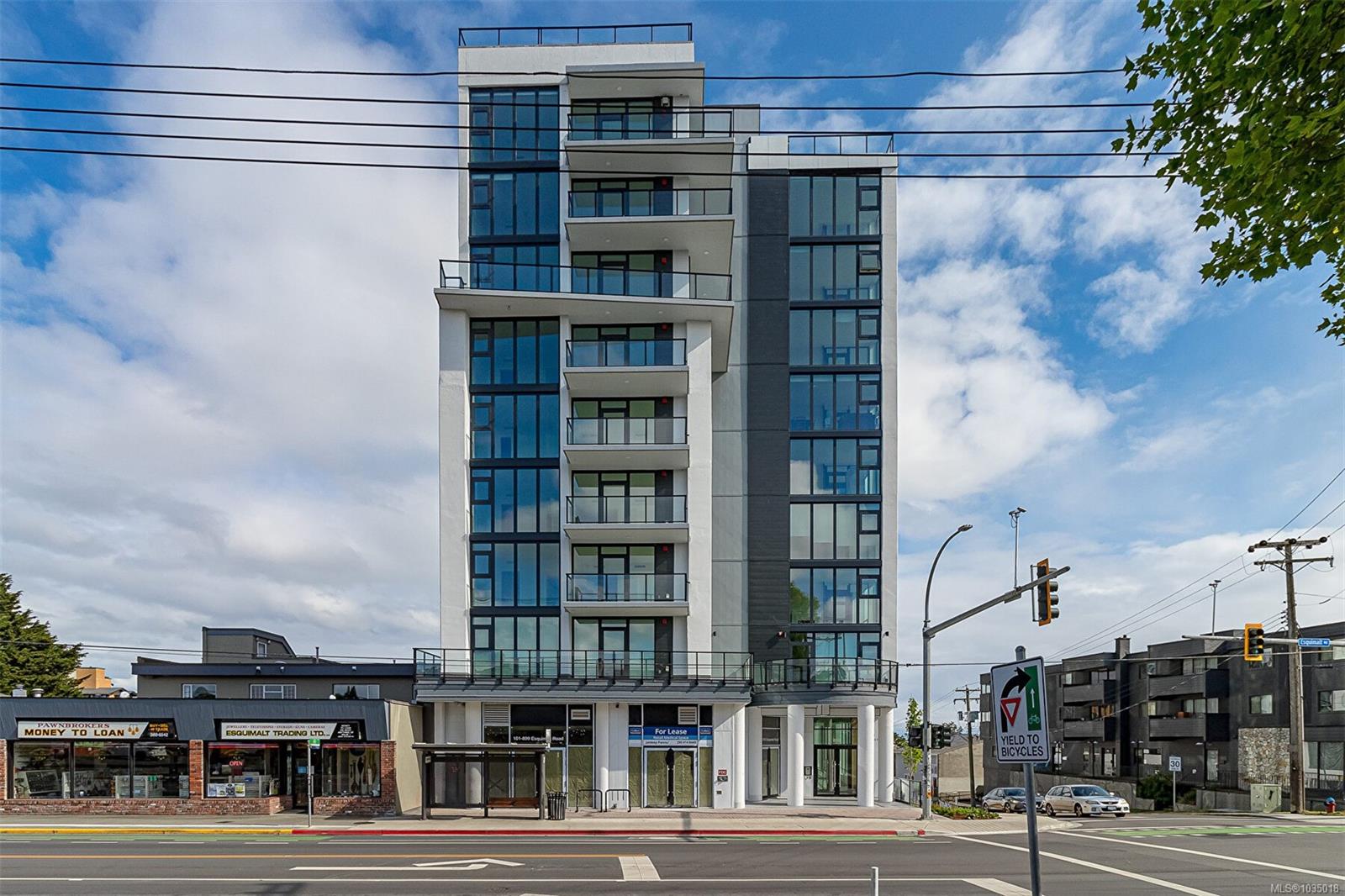 Modern six story glass front condo building with balconies on a busy street storefronts at ground level