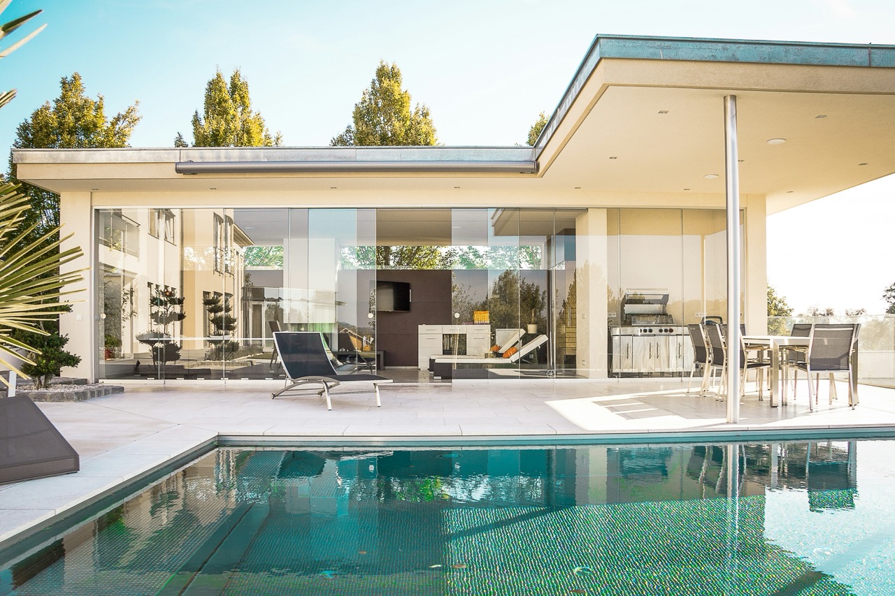 florianschmidingerb79nOqf95IunsplashLargejpeg | Apartments Homes Suites for Rent Victoria BC Modern glass walled house with a spacious patio lounge chairs and an outdoor dining area beside a blue tiled pool